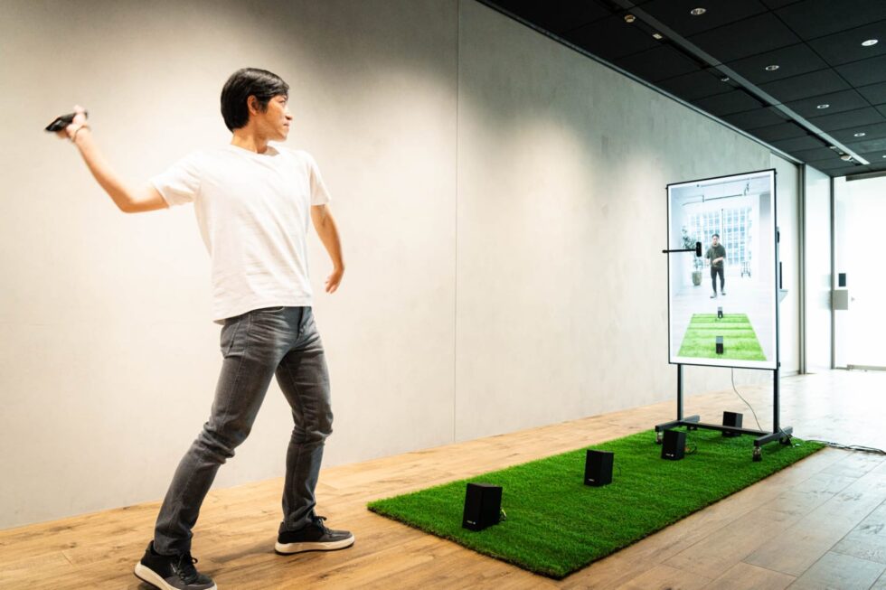 XRキャッチボールを体験する中川テルヒロ。液晶画面に映る男性に向かって、ボールを投げる動作をしている。