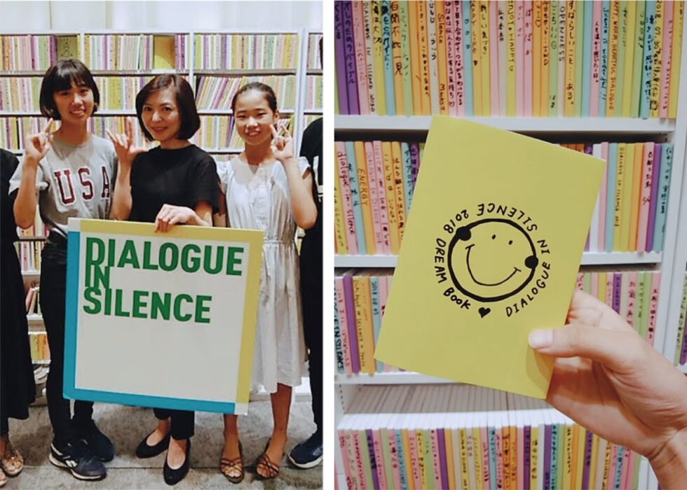 「DIALOGUE IN SILENCE」体験時の2枚の写真。1枚目、アテンドと小島の記念写真。手話で「I love you」をして笑顔でポーズ。2枚目、たくさんの本が並べらた本棚の前で、手書きでニコちゃんマークが書かれた本を持っている。
