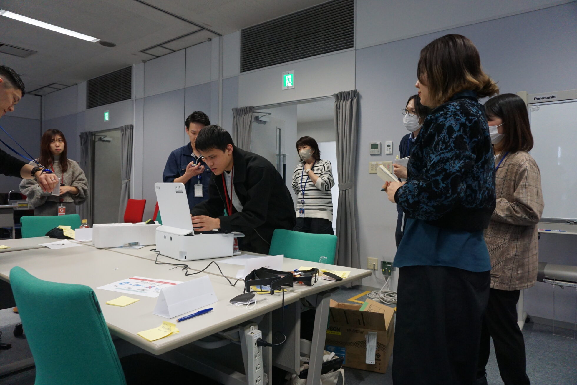 視覚障害リードユーザーが、プリンターの上部を開き、手で確認しながらスキャンをしようとしている。その様子を囲むように参加者が観察している。