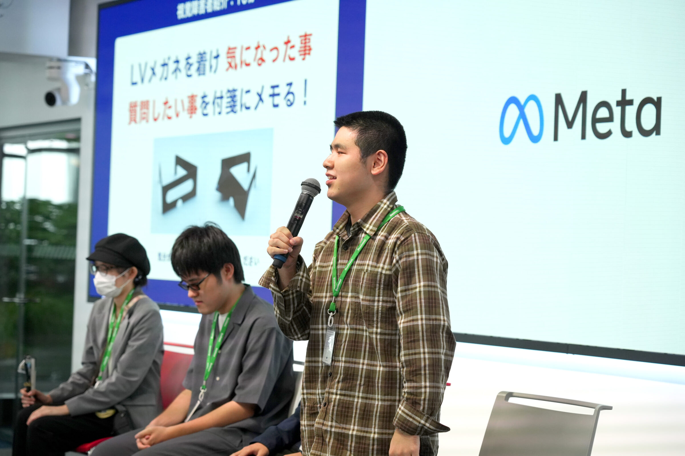 視覚障害リードユーザーが会場前方に立ち、マイクを持って自己紹介をしている。