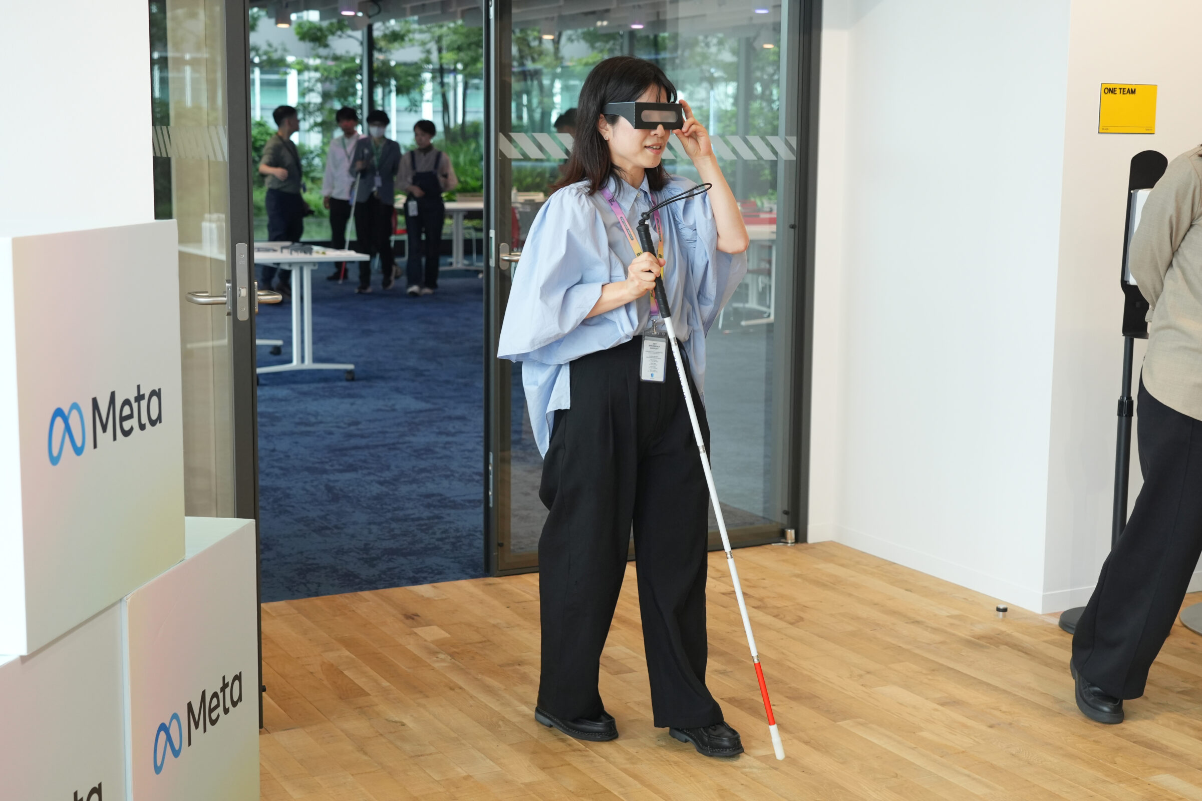 ロービジョン体験眼鏡を着け、白杖を持った参加者がMetaオフィス内を歩き、見えにくさを体験している様子。