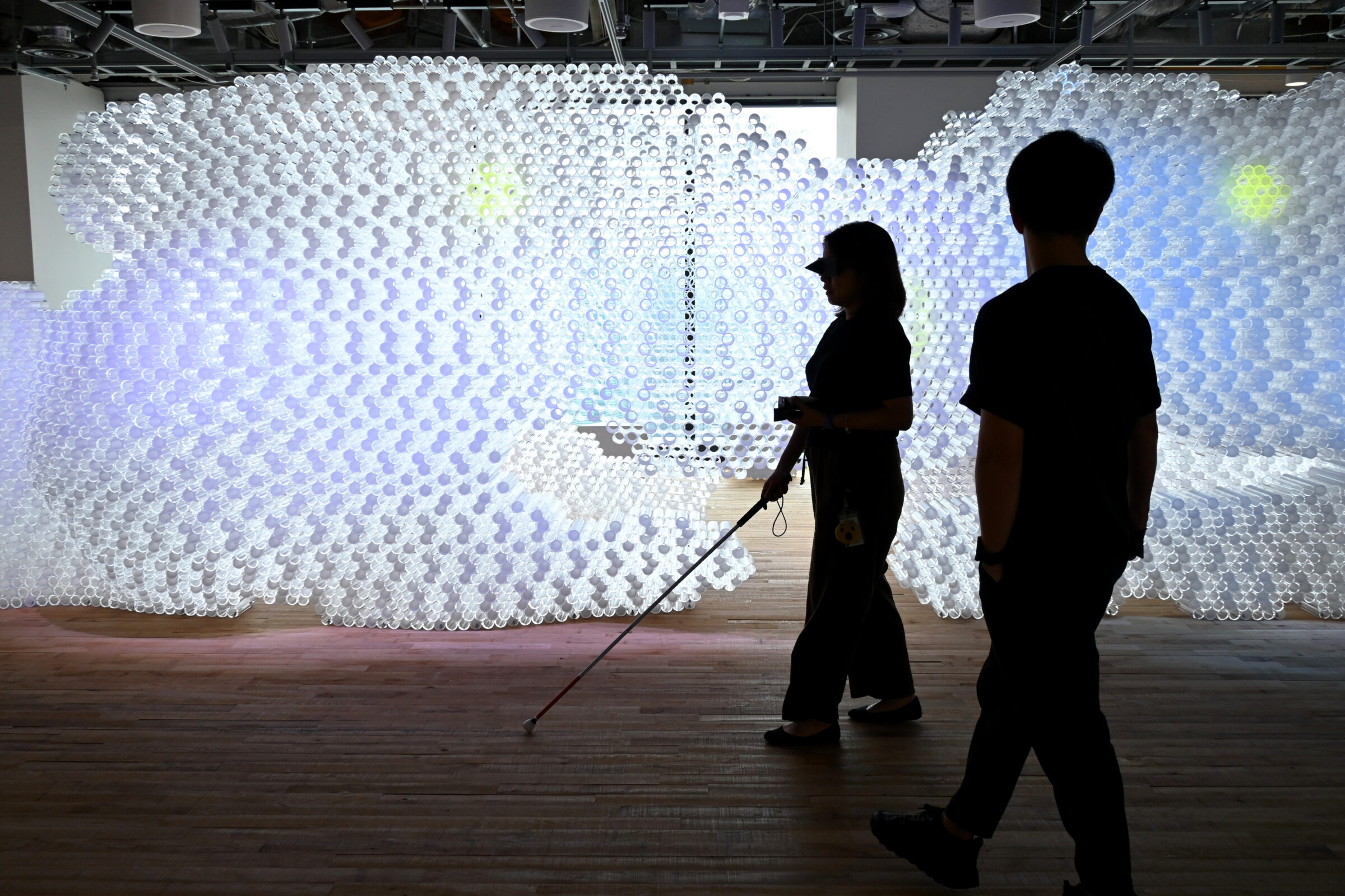 白杖を持った参加者が、光る立体アートが展示されたMetaオフィス内を歩いている様子。